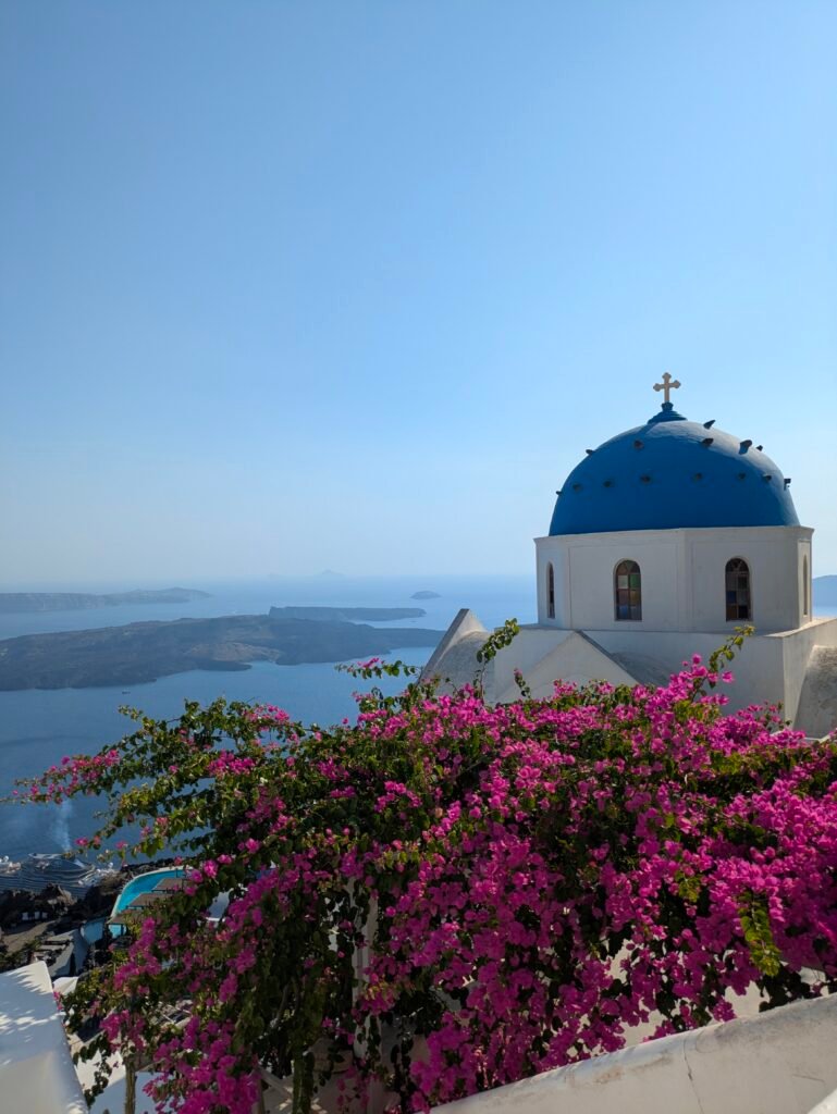 cupola blu e chiesa bianca in grecia con fiori fucsia